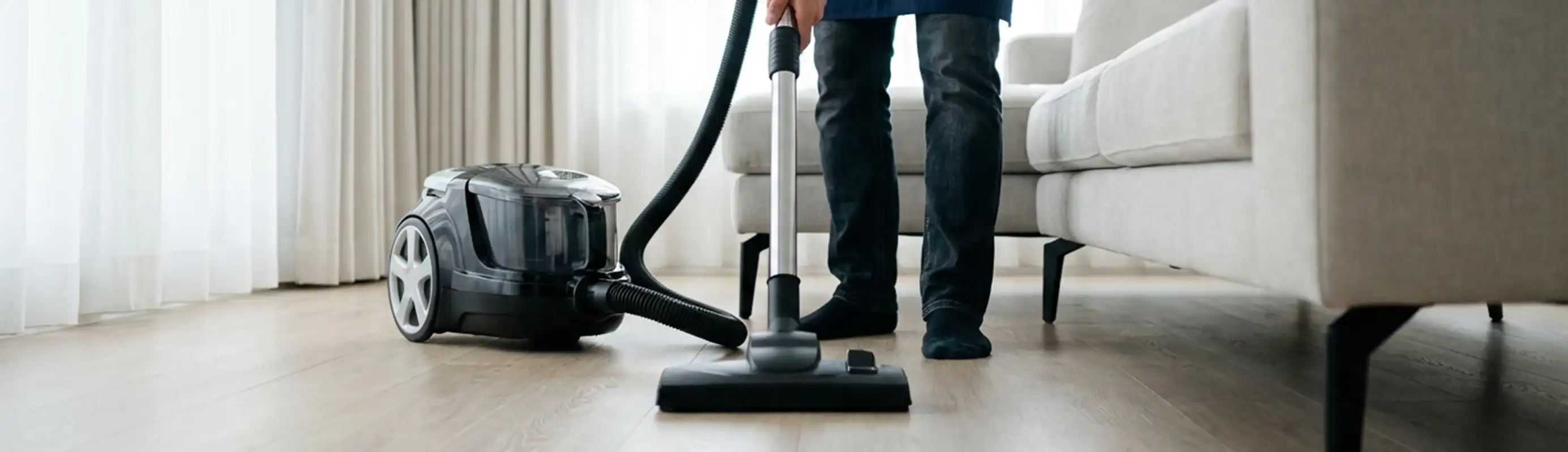 Professional house cleaner vacuuming a living room floor with a canister vacuum cleaner, Baltimore, MD.