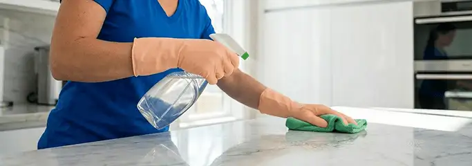 Maid service worker spraying and wiping a kitchen countertop with a microfiber cloth for sanitizing, Baltimore, MD.