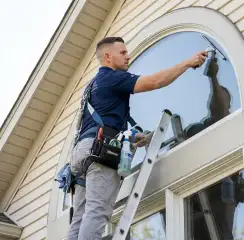 Professional window cleaner on a ladder using a squeegee to clean an exterior arched window, Baltimore, MD.