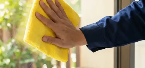 House cleaner wiping a glass window with a yellow microfiber cloth for streak-free cleaning, Baltimore, MD.